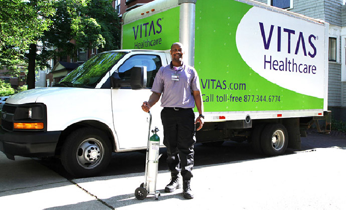 A VITAS home medical equipment team member holds an oxygen tank next to his vehicle
