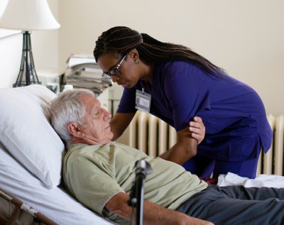 A VITAS nurse helps a man sit up in bed