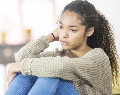 A teenaged girl rests her arm on her knees as she stares into the distance