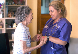 Una enfermera estrecha las manos de una paciente mientras sonríen