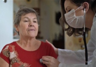 A healthcare professional wearing a face mask uses a stethoscope with a female patient