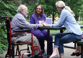 A VITAS care team member sits at an outdoor picnic table with a patient and his daughter