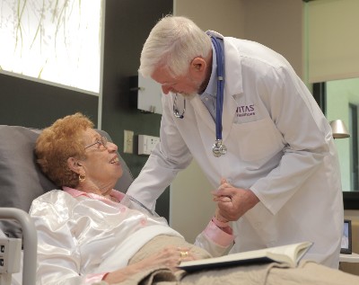 A VITAS doctor talks with a patient in a bed at a hospice inpatient unit