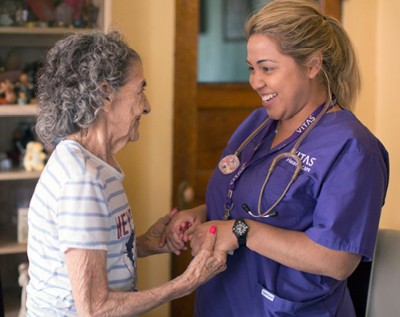 Una enfermera de VITAS y una paciente tomadas de la mano y sonriendo