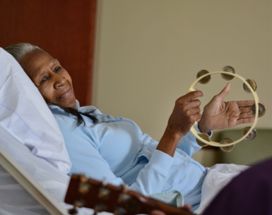 A woman lying in a patient bed plays the tambourine