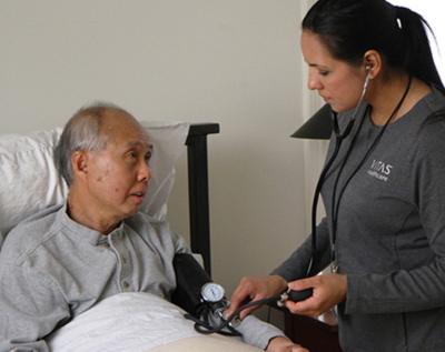 Một thành viên nhóm của VITAS đang đo huyết áp cho bệnh nhân khi ông này đang nằm trên giường