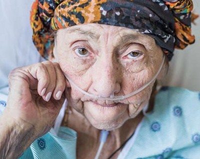 A woman sits at her husband's bedside as he rests while using supplemental oxygen