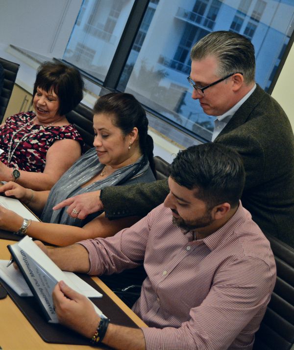 A group of people sits at a conference table reviewing paperwork