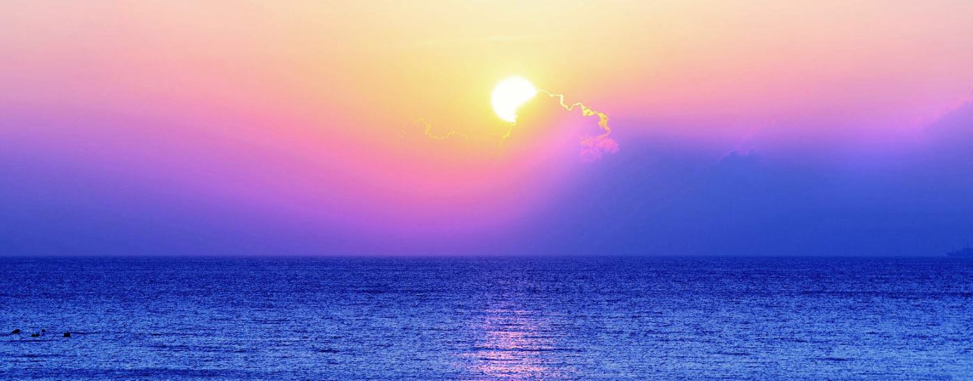The sun sets over a purple-blue ocean.