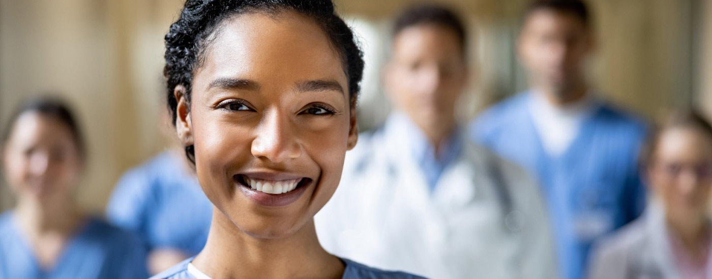 A nurse smiles, she is standing in front of a group of other healthcare workers