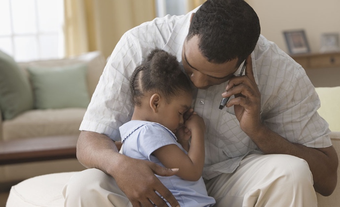 A man talks on the phone while holding his young daughter