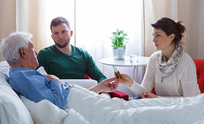 Una pareja habla con un hombre mayor que está en cama