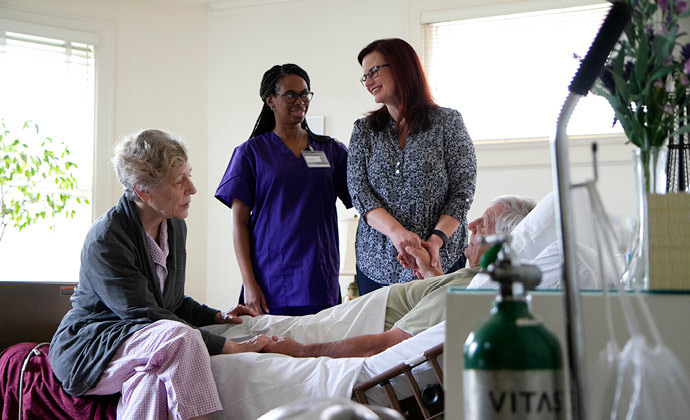 Napapaligiran ang isang lalaking nakahiga sa kama ng kanyang asawa, anak, at nurse ng VITAS hospice