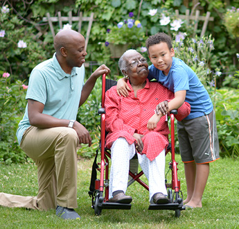 女士在戶外坐在輪椅上休息，她的孫子抱著她