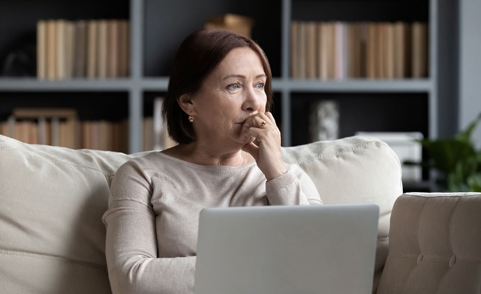 Isang babae na nakaupo sa sofa, gumagamit ng laptop at nakatingin sa malayo