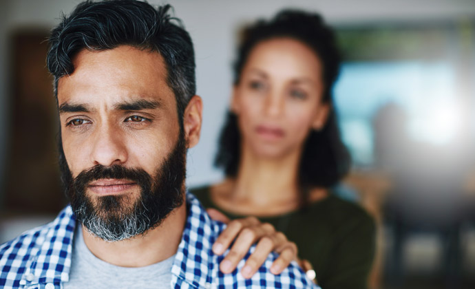 A woman rests her hand on a man's shoulder as he grieves