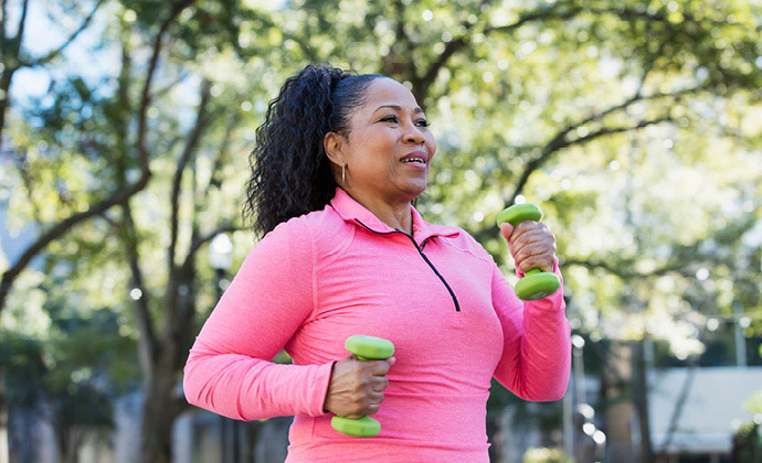 A woman power-walks outdoors while holding a small weight in each hand