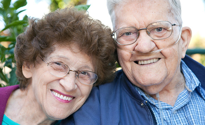 A man wearing oxygen tubes smiles next to his wife