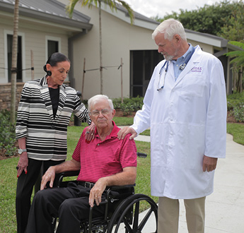 Một người đàn ông ngồi xe lăn đang được bác sĩ và vợ mình giúp đỡ