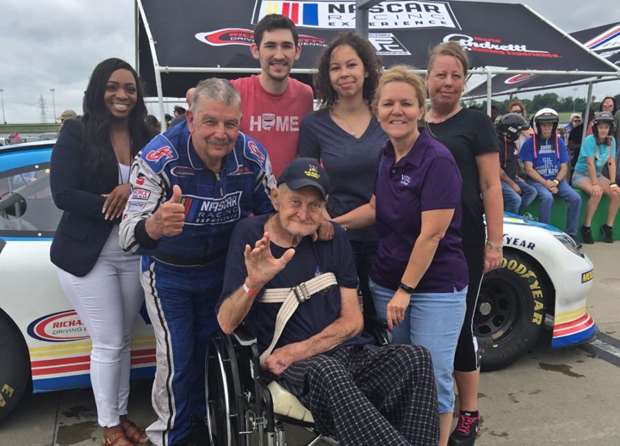 Ronald sits next to the NASCAR racecar surrounded by his VITAS team