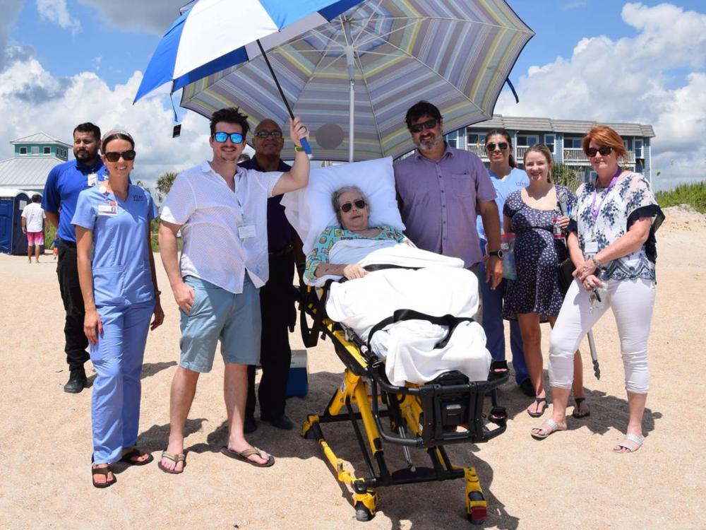 The team poses with Deirdre in her hospital bed at the beach, helping shelter her from the hot Florida sun with an umbrella