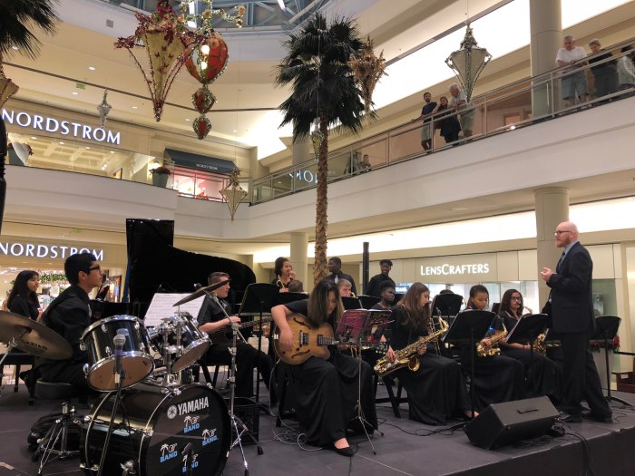 A group of students play guitar, saxophones, drums and other instruments on stage at the mall