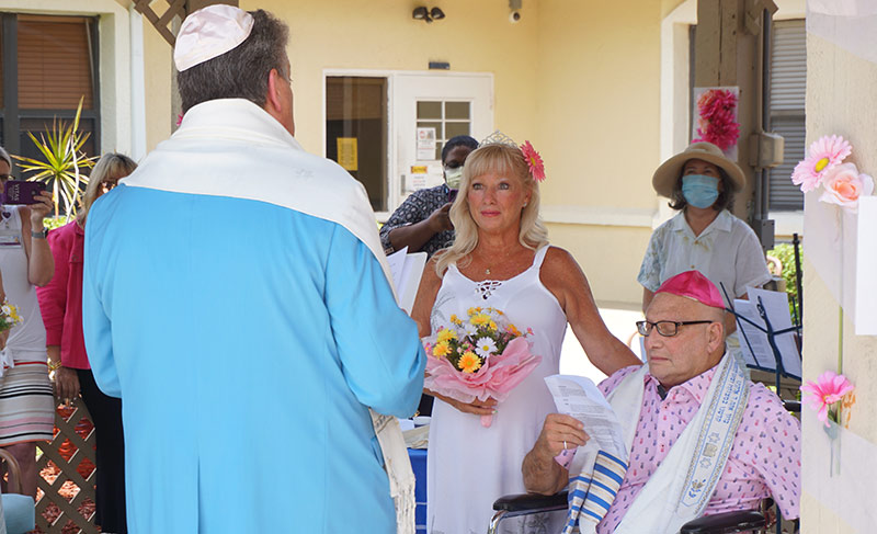 The couple and celebrant, with guests nearby, were outside for the ceremony