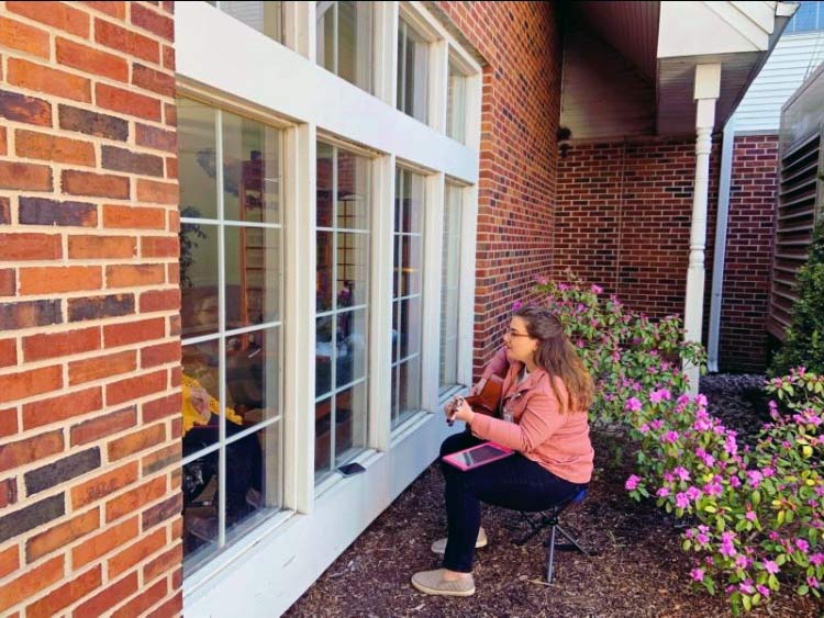 Mia plays outside a window for a patient listening by phone inside