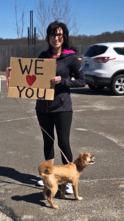 VITAS Representative Lisa Gould holds her dog's leash and a sign saying "We Love You" outside an assisted living facility