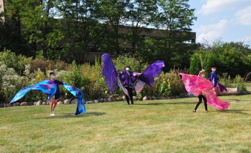 Three dancers perform, each wearing large cloth butterfly wings on their arms