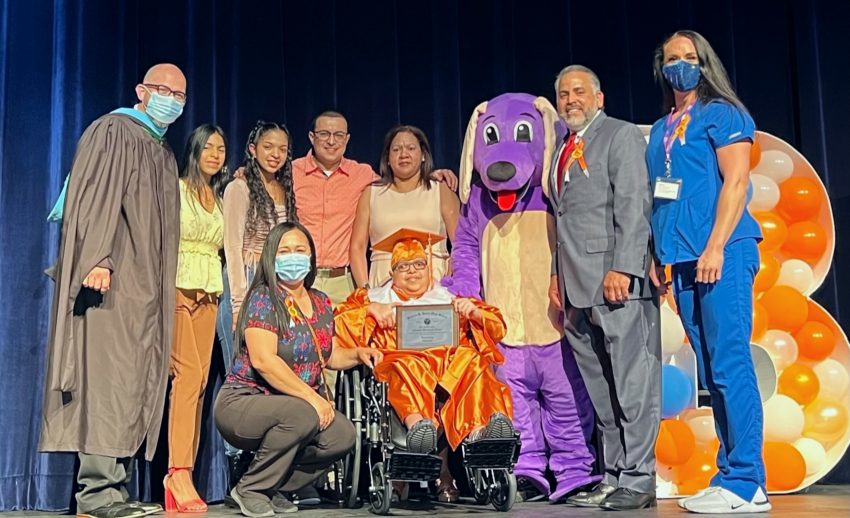 Abraham Maldonado at center stage with his diploma, surrounded by family and members of his VITAS care team