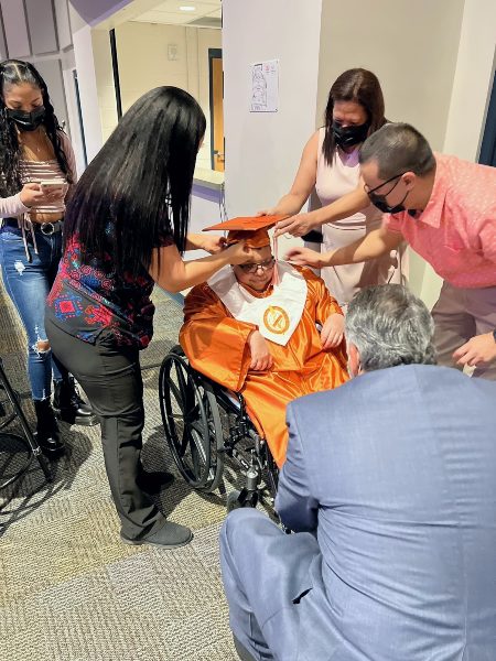 VITAS patient Abraham Maldonado, at center in wheelchair, is dressed in cap and gown and surrounded by family and VITAS team members