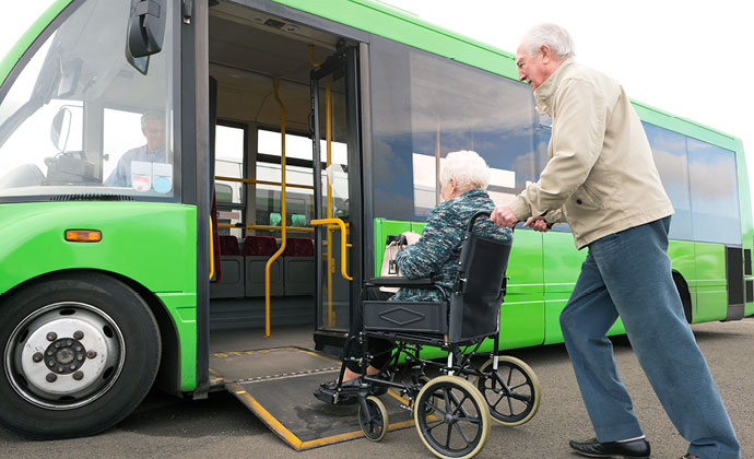 Un cuidador ayuda a una paciente en silla de ruedas a subir a un autobús de traslado
