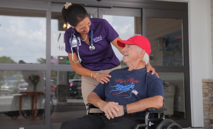 Una médica de VITAS habla con un paciente veterano en silla de ruedas al aire libre