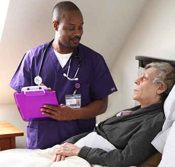 Một nhà cung cấp dịch vụ của VITAS đang đứng cạnh một giường bệnh và trò chuyện với bệnh nhân