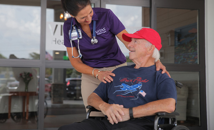 Una proveedora de VITAS habla con un paciente en silla de ruedas al aire libre