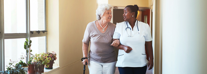 Caretaker assists patient walking down hallway