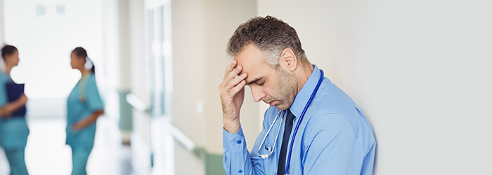 Doctor leaning against wall rubbing forehead