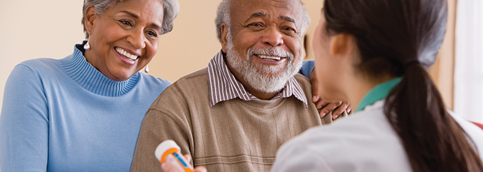 Man and Wife holding medications smiling with caretaker