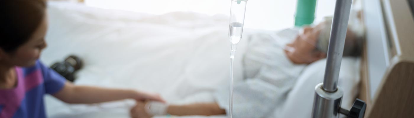 A family member holds the hand of a patient in a hospital bed