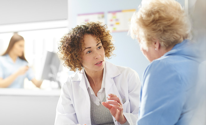 A physician seated at a table with a laptop computer talks with a patient