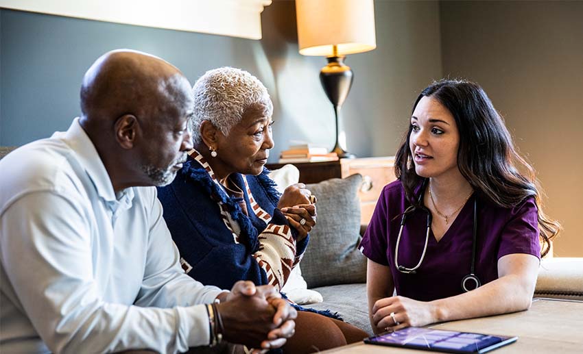 A nurse sits at a table and talks with an elderly husband and wife