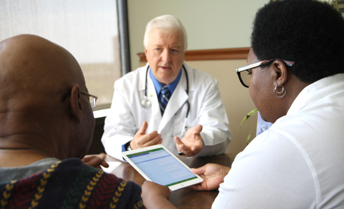 A physician talks with a couple in his office as they look at information on an iPad
