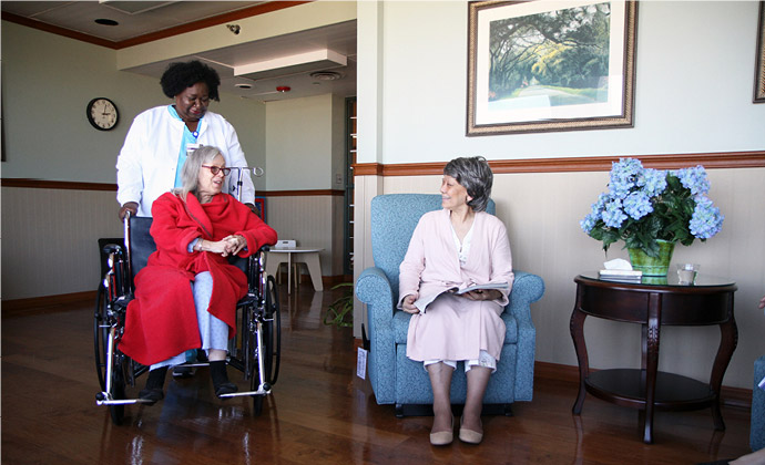 Una enfermera ayuda a una paciente en silla de ruedas mientras esta habla con otra residente