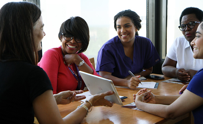 Profesionales de servicios de asistencia médica hablan en una mesa de conferencias mientras una de las miembros muestra información en una tablet
