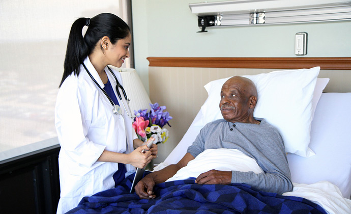 Una médica de VITAS habla con un paciente que está acostado en la cama