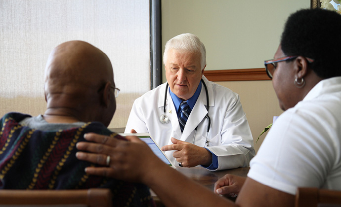 Un médico de VITAS comparte información en una tablet con una pareja que está sentada en su consultorio