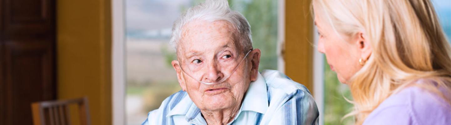 Un hombre mayor con una cánula nasal para la administración de oxígeno habla con su hija en su casa