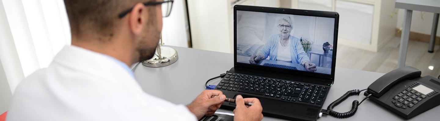 A physician talks with a caregiver via a laptop videoconference