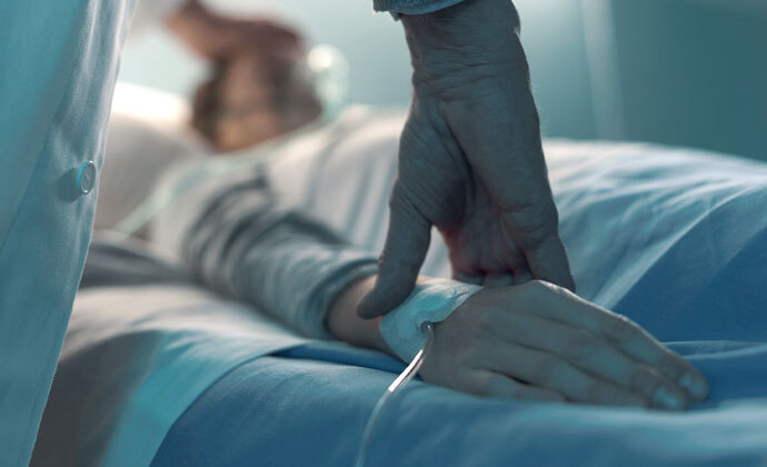 An aide comforts a patient as he lies in bed